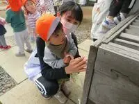 写真：先生と一緒に賽銭箱の前で手を合わせている子