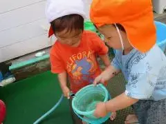 写真：バケツを持つ子にホースで水を入れている子