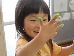 写真：絵の具が手について色とりどりになった右手を楽しそうにみる子