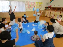 写真：青いビニールシートの周りを親が囲んで、中で子供が遊んでいる様子