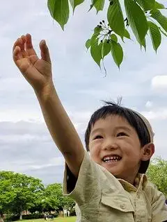写真：満面の笑顔で公園の木の枝に手を伸ばしている子