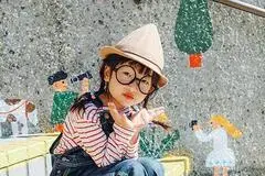 写真：市役所のウォールアートをバックに黒い大きな丸眼鏡と赤いボーダーの服が印象的な子