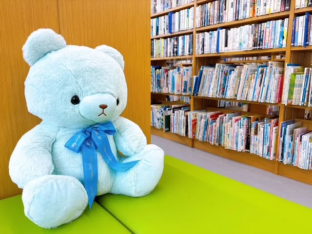雑誌架のいすに座るクマのぬいぐるみ