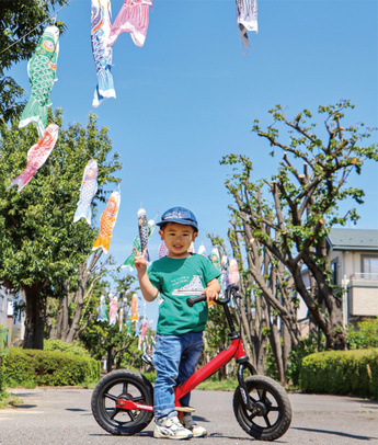 こいのぼりが掲揚された通りの真ん中で自転車の傍らで少年がピースをしている写真